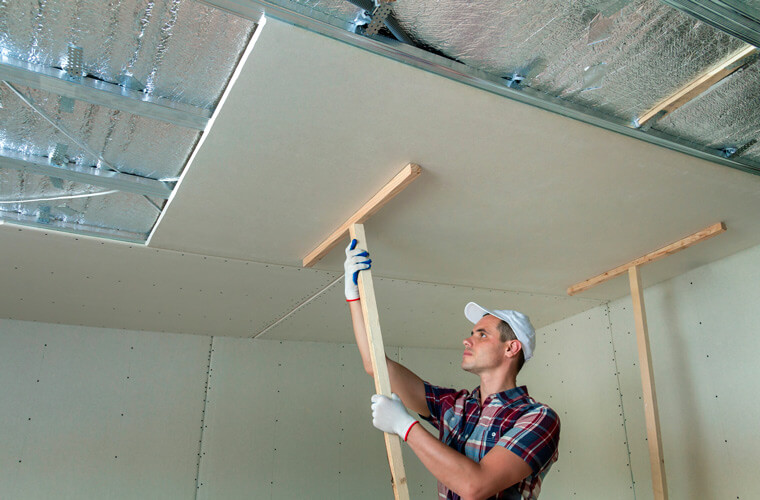 man hanging drywall on ceiling